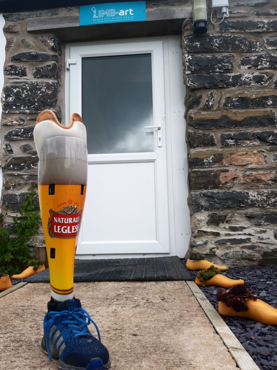 A prosthetic leg cover in a Carlsberg beer design shown with trainer shoe with writing Naturally Legless
